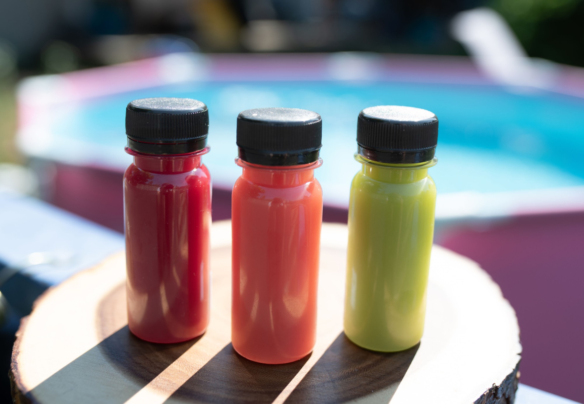 Three bottles of Last Bite fresh juice in red, orange and green on a wooden board